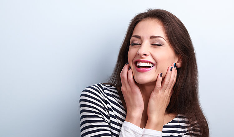 Brunette woman smiling with her eyes closed and her hands on her cheeks