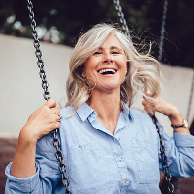 a woman with partial dentures smiling on a park swing