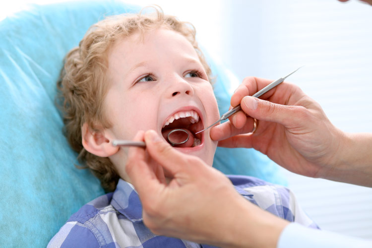 young boy with his mouth open getting a back-to-school dental exam