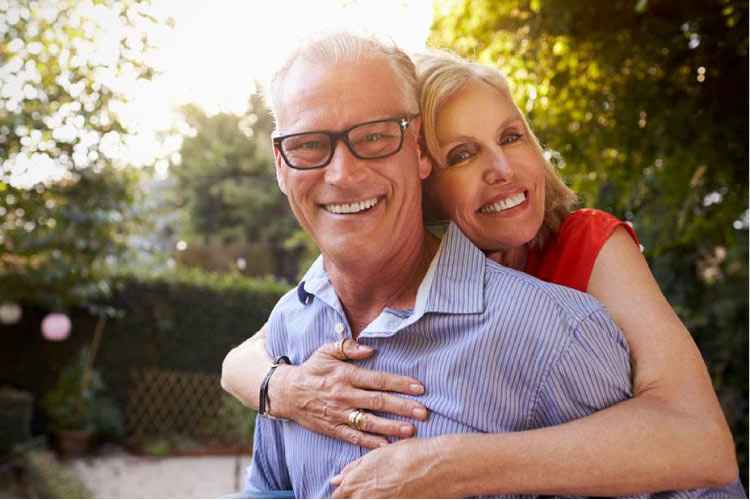 senior couple hugging and smiling after learning about the benefits of dentures