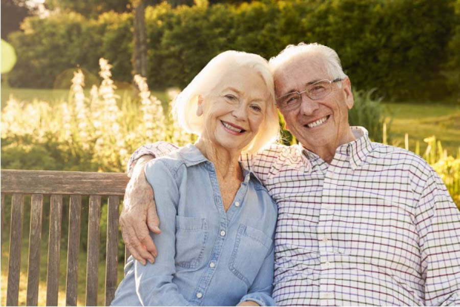 senior couple sitting on a bench hug and smile after learning how to adapt to dentures