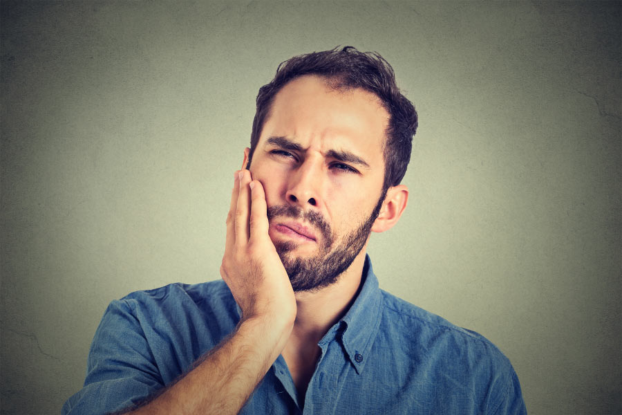 bearded man holds his jaw with pain from gum disease