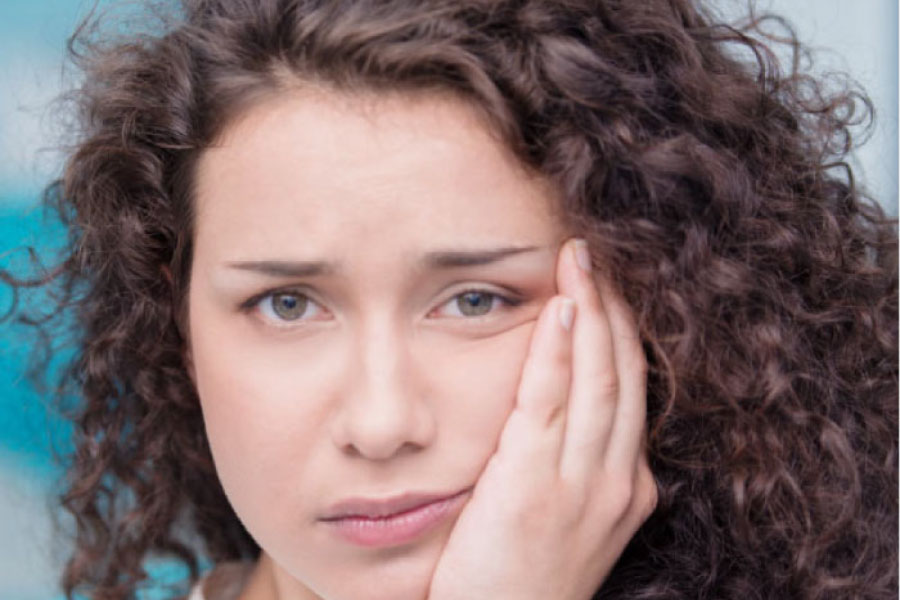 young woman holds her jaw in pain after wisdom teeth removal