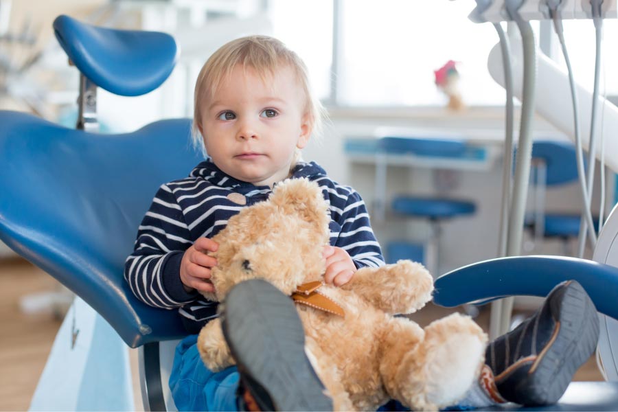 young boy sitting in the dentist chair holding a teddy bear