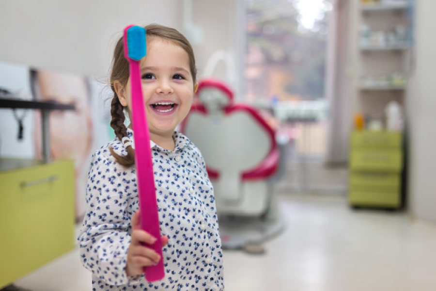 young girl holds up a giant toothbrush at the dentist office.