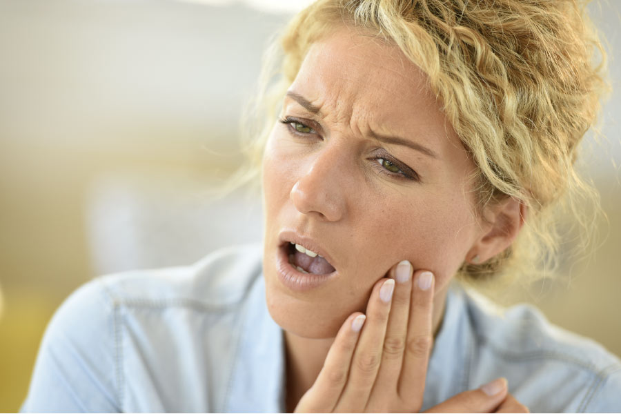 blond woman holds her jaw in pain with a serious toothach