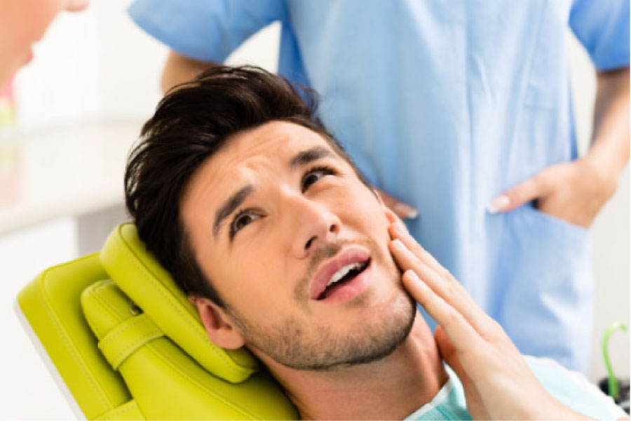 man in the dentist chair holds his cheek in pain before root canal therapy